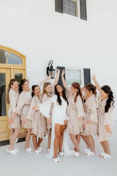 a group of women standing next to each other in front of a white building holding their arms up