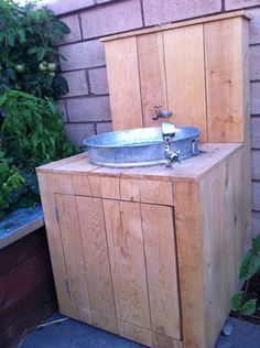 a wooden cabinet with a metal bowl on it's top, and a brick wall in the background