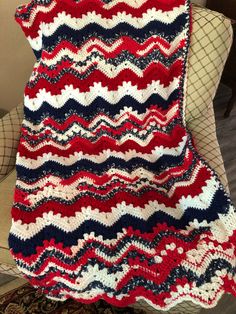 a red white and blue crocheted blanket sitting on top of a chair next to a pillow