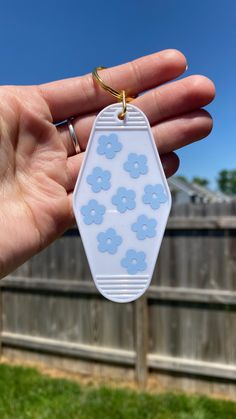 a hand holding a white and blue flower shaped keychain in front of a fence