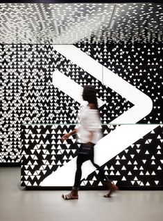 a woman walking in front of a black and white wall