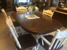 a dining room table with white chairs and flowers in a vase on the centerpiece