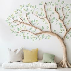 a white couch sitting under a tree with green leaves painted on it's wall