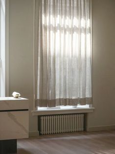 an empty room with a window, radiator and white curtains on the windowsill