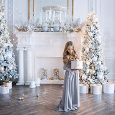 a beautiful young woman holding a present in front of christmas trees