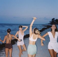 four women are dancing on the beach at night with their arms up in the air