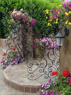 an iron gate with flowers growing out of it next to a stone wall and steps