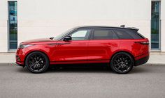 a red range rover parked in front of a white building with black wheels and rims