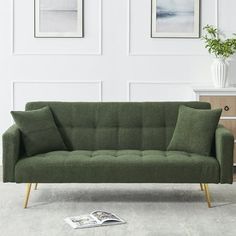 a green couch sitting on top of a white floor next to a wooden table and two framed pictures