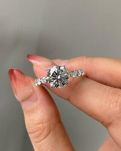 a woman's hand holding an engagement ring with three stones on it, in front of