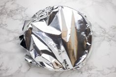 a round metal object sitting on top of a white marble countertop covered in foil