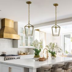 a kitchen with white cabinets and gold pendant lights hanging from the ceiling over the island