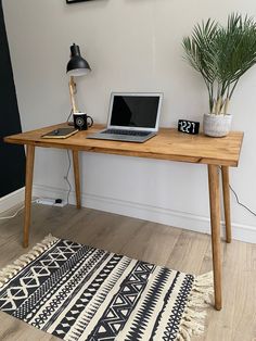 a laptop computer sitting on top of a wooden desk next to a potted plant