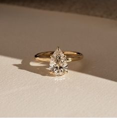 a yellow gold engagement ring with a pear shaped diamond on the side, sitting on a white surface