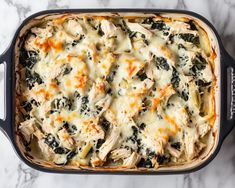 a casserole dish with chicken, spinach and cheese in it on a marble surface