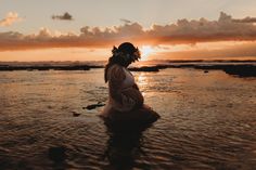 a pregnant woman standing in the water at sunset