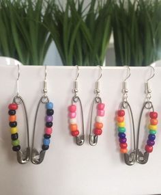 four pairs of colorful beaded earrings hanging from hooks on a white surface next to a potted plant