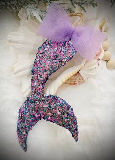 a mermaid tail with pink and purple sequins on it, next to shells