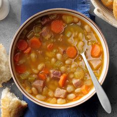 a bowl of soup with ham, beans and carrots on a blue napkin next to bread