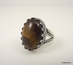 Large, bold and simply stunning. This large sterling silver tiger's eye ring is perfect for the individual who loves detail in every aspect of their lives. A large 18 x 13 mm tiger's eye cabochon is nestled in a beautiful sterling silver base, which has a victorian filigree design that adds to the beauty of the stone. The ring base is 3mm wide and 0.9mm thick, giving it a sturdy, yet very comfortable feel. This ring is available in a size 7. Tiger's eye is the gemstone associated with the 9th ye Brown Oval Gemstone Rings, Elegant Brown Rings With Natural Stones, Brown Sterling Silver Cabochon Ring, Brown Sterling Silver Ring With Cabochon, Brown Oval Cabochon Rings, Sterling Silver Rings With Brown Natural Stones, Brown Sterling Silver Rings With Natural Stones, Oval Brown Rings With Natural Stones, Brown Oval Rings With Natural Stones