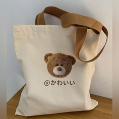 This Adorable Street-Style Japanese Kanji Cute Teddy Tote Bag Is A Versatile Design That Combines Youthful Style With Practical Functionality, Making It A Perfect Companion For Everyday Use. The Photo Embossed Teddy Bear Image And The Lettering In Japanese Kanji Which Translates To The Word “@Cute” Perfectly Nails The Kawaii Aesthetic! Crafted From Durable Canvas, It Offers Ample Space For Carrying Essentials Like Books, Groceries, Or Everyday Items. 100% Canvas Kanji Lettering Spells “Cute” In Cute Beige Shoulder Bag For School, Cute Brown Bag For Daily Use, Cute Beige Bags For Daily Use, Cute Beige School Shoulder Bag, Cute Brown Bags For Daily Use, Cute Cream Shoulder Bag For School, Cute Canvas Bag For Daily Use, Beige Pouch Canvas Bag For School, Cute Canvas Shoulder Bag For Daily Use