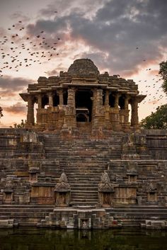 birds flying in the sky over an ancient structure with steps and pillars on it's sides