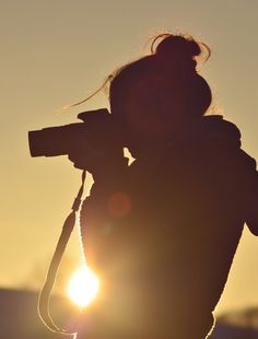 a person holding a camera in their hand and the sun shining behind them is black and white