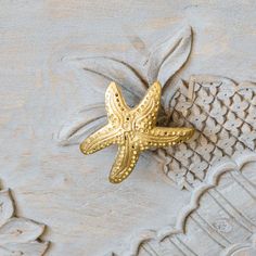 a gold starfish brooch sitting on top of a piece of white wood with intricate designs