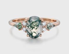 a green and white stone ring with three diamonds on the side, set in rose gold