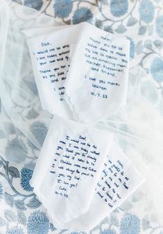 three embroidered napkins with words on them sitting on a floral print cloth covered tablecloth