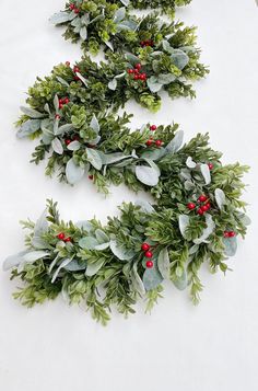 two christmas wreaths with red berries and green leaves on white tablecloth, top view