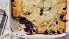 a casserole dish with blueberries in it on a white cloth next to a fork