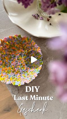 a white plate topped with flowers next to a vase filled with purple and yellow flowers