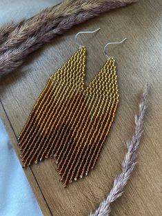 a pair of gold beaded earrings sitting on top of a wooden table next to some feathers