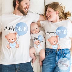 a man and woman laying on top of a bed next to a baby wearing shirts that say daddy bear