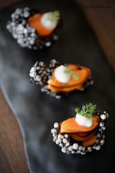 three small carrots are on a black plate with pearls and garnishes