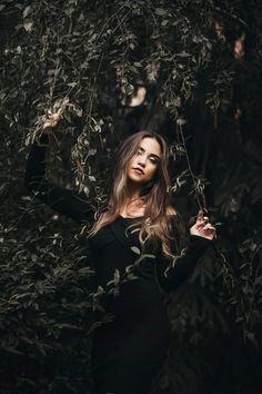 a woman standing in front of trees with her hands on her hips and looking at the camera