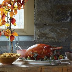 a large turkey sitting on top of a table next to a bowl of fruit and vegetables