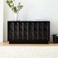 a black cabinet sitting on top of a wooden floor next to a vase with flowers