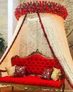 a red couch sitting in front of a white canopy bed with flowers on the headboard