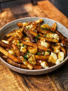 a bowl filled with french fries covered in gravy on top of a wooden table