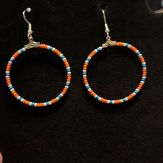 two pairs of orange, blue and white beaded hoop earrings on a black surface