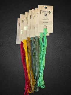 five tassels of different colors and sizes on a black background with the tag for each string