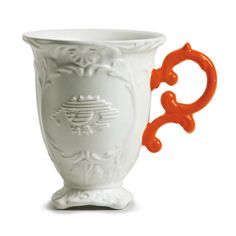 a white cup with an orange handle is shown in front of a white background and has ornate designs on it