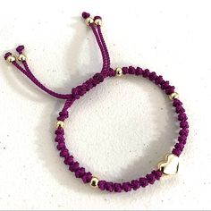 a purple bracelet with two gold hearts on it and a white beaded cord around the clasp