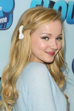 a young blonde girl with long hair and a flower in her hair smiles at the camera