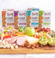 three boxes of oat crackers next to an assortment of fruit and nuts on a wooden board