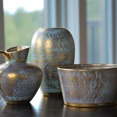 three vases and a bowl sitting on a table in front of a large window