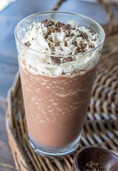 a chocolate drink with whipped cream and chocolate shavings on the top is sitting on a wicker tray