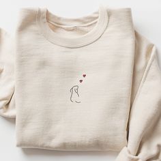 a white sweater with hearts on it and a cat embroidered on the front, sitting against a white background